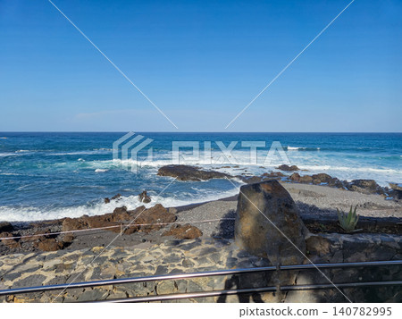 Rocky Ocean Shoreline Under Clear Blue Sky Rocky Ocean Shoreline Under Clear Blue Sky 140782995