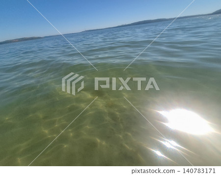 Sunlit Calm Sea Water With Distant Shoreline Sunlit Calm Sea Water With Distant Shoreline 140783171