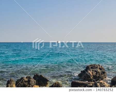 Rocky Seashore with Boat on Calm Blue Water Rocky Seashore with Boat on Calm Blue Water 140783252