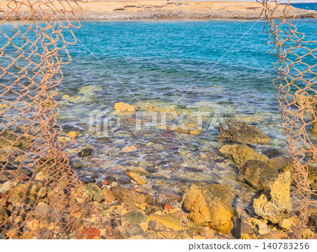 Rocky shoreline framed by rusty fishing net Rocky shoreline framed by rusty fishing net 140783256