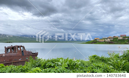 Rusting boat beside mountain lake shoreline. Abandoned vessel rests near Tabatskuri Lake in Georgia with distant snowy peaks Rusting boat beside mountain lake shoreline. Abandoned vessel rests near Tabatskuri Lake in Georgia with distant snowy peaks 140783648