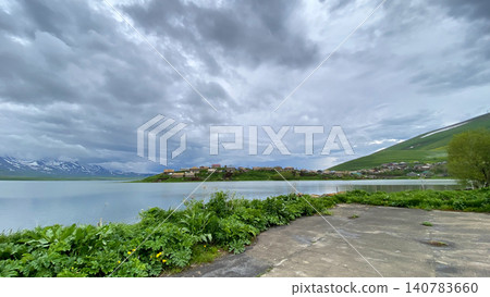 Mountain lake and village under stormy sky. Scenic view of Tabatskuri Lake in Georgia with rural settlement 140783660