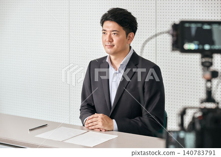 A Japanese businessman in his 30s is recording video in front of a camera in a filming studio. A Japanese businessman in his 30s is recording video in front of a camera in a filming studio. 140783791