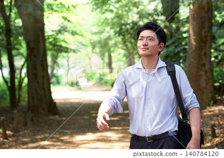 A Japanese male office worker in his 30s, with a relaxed expression, walks through a refreshing, lush green park on a hot summer day, smiling. A Japanese male office worker in his 30s, with a relaxed expression, walks through a refreshing, lush green park on a hot summer day, smiling. 140784120