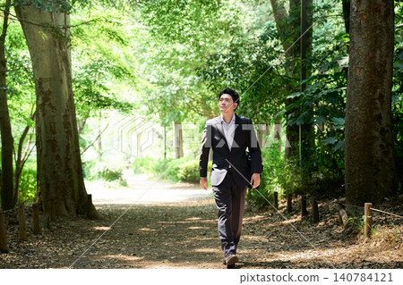 A Japanese businesswoman in her 30s, on her outside sales job, is strolling along a shady path in a lush park, looking up at the trees and smiling. A Japanese businesswoman in her 30s, on her outside sales job, is strolling along a shady path in a lush park, looking up at the trees and smiling. 140784121