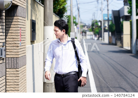 A Japanese male office worker in his 30s, who works outside sales, walks down a residential street in the hot summer. A Japanese male office worker in his 30s, who works outside sales, walks down a residential street in the hot summer. 140784124