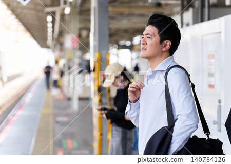 一位三十多歲的日本男上班族在炎熱的夏天於車站月台上等候火車。 一位三十多歲的日本男上班族在炎熱的夏天於車站月台上等候火車。 140784126