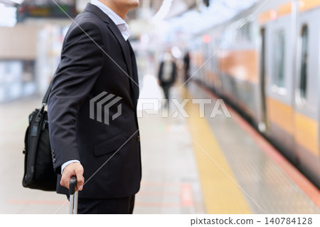 一位面容模糊的日本商人，年齡在三、四十歲之間，出差在外，提著行李箱在月台上等火車。 140784128
