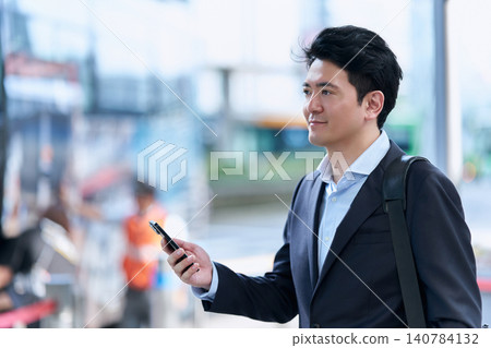 一名三十多歲的日本男子,是公司職員,在公車站面帶微笑,低頭看著自己的智慧型手機。 一名三十多歲的日本男子,是公司職員,在公車站面帶微笑,低頭看著自己的智慧型手機。 140784132