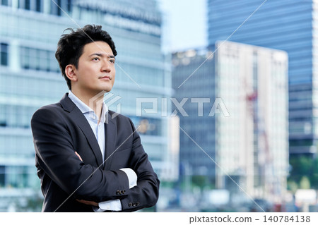 一位三十多歲的日本商人雙手交叉抱在胸前,凝視著城市辦公區遠方。 一位三十多歲的日本商人雙手交叉抱在胸前,凝視著城市辦公區遠方。 140784138