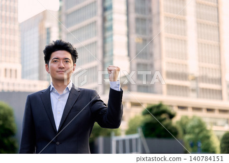 在熙熙攘攘的城市辦公區,一位微笑的日本商人傍晚時分直視鏡頭,做出勝利的手勢。 在熙熙攘攘的城市辦公區,一位微笑的日本商人傍晚時分直視鏡頭,做出勝利的手勢。 140784151