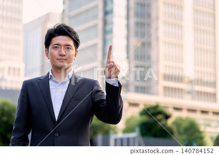 In a bustling city office district in the evening, a businessman in his 30s makes a suggestion and gives directions while holding up his index finger. In a bustling city office district in the evening, a businessman in his 30s makes a suggestion and gives directions while holding up his index finger. 140784152