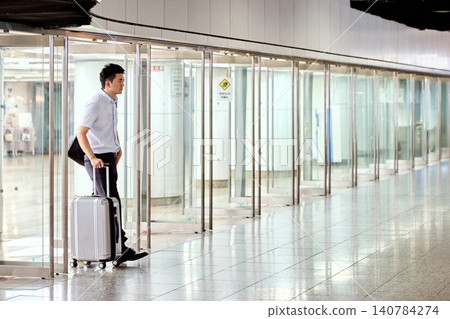 A businessman, carrying a suitcase, walks through an underground passage with a series of glass doors, on his way to a business trip. A businessman, carrying a suitcase, walks through an underground passage with a series of glass doors, on his way to a business trip. 140784274