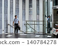 A Japanese male office worker in his 30s, wearing a short-sleeved shirt, walks up the stairs of an office building while commuting for work. 140784278