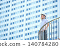 A Japanese man in his 30s, wearing a helmet and a short-sleeved shirt, is a site supervisor, looking up at a skyscraper against the backdrop of a city skyline. 140784280