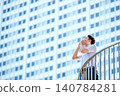 A Japanese businessman in his 30s, wearing a short-sleeved shirt, shouts a message loudly from a terrace in a high-rise building district. 140784281