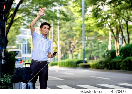 一名男性上班族提著行李箱,在出差途中用智慧型手機上的叫車軟體預訂了一輛計程車,正在等車。 一名男性上班族提著行李箱,在出差途中用智慧型手機上的叫車軟體預訂了一輛計程車,正在等車。 140784283