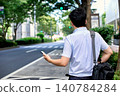 The back view of a male office worker waiting for a taxi he ordered using a smartphone app on the street while commuting for work. 140784284