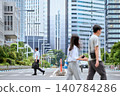 A Japanese businessman in his 30s, working on a holiday, walks across a crosswalk on a city street, passing by people. 140784286