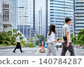 A Japanese man in his 30s, a company employee, is walking across a pedestrian crossing in a high-rise building district of a city on a public holiday, when a couple on a date crosses the street. 140784287