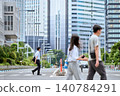 A Japanese businessman in his 30s wearing a short-sleeved shirt walks across a crosswalk on a city street, passing by people. 140784291