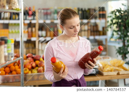 Female shopper chooses peach juice or tomato juice while shopping in supermarket Female shopper chooses peach juice or tomato juice while shopping in supermarket 140784537