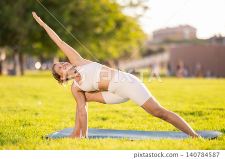 Girl in park on green grass of lawn performs Utthita Parshvakonasana Girl in park on green grass of lawn performs Utthita Parshvakonasana 140784587