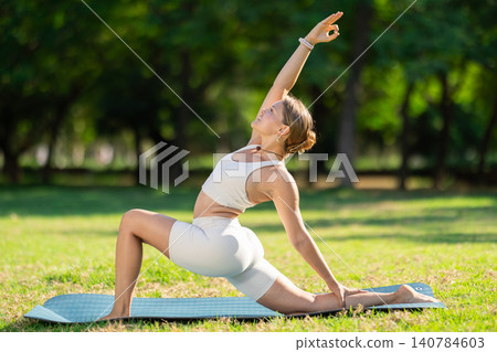 Young yogini performing Crescent Low Lunge Pose in summer park Young yogini performing Crescent Low Lunge Pose in summer park 140784603