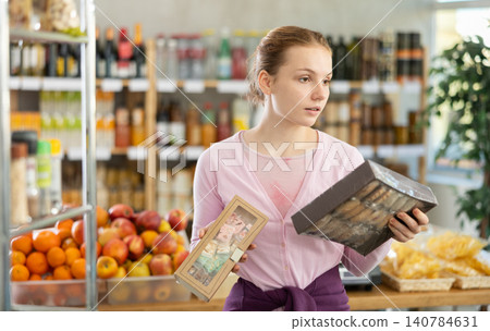Woman chooses sweet cookies while shopping in grocery supermarket Woman chooses sweet cookies while shopping in grocery supermarket 140784631
