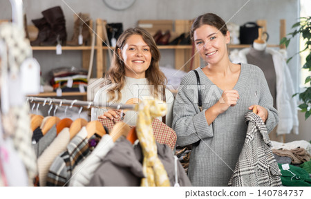 Two focused young girl clients carefully looking something for autumn-winter season in clothing mall. Winter sales Two focused young girl clients carefully looking something for autumn-winter season in clothing mall. Winter sales 140784737