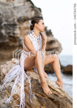 Girl on seashore in sexy and revealing carnival costume sitting on stone Girl on seashore in sexy and revealing carnival costume sitting on stone 140784788
