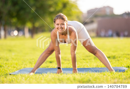 Cheerful girl practicing Prasarita Padottanasana on green summer glade Cheerful girl practicing Prasarita Padottanasana on green summer glade 140784789