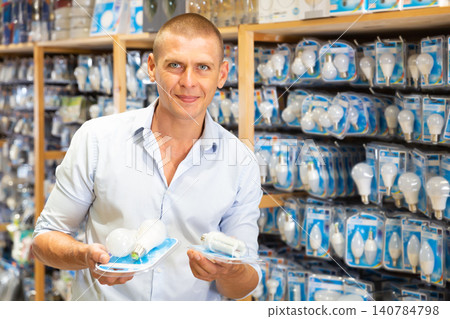 Man choices energy saving lamp at hardware store Man choices energy saving lamp at hardware store 140784798