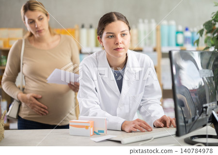Pharmacist checking stock availability for pregnant woman with prescription Pharmacist checking stock availability for pregnant woman with prescription 140784978
