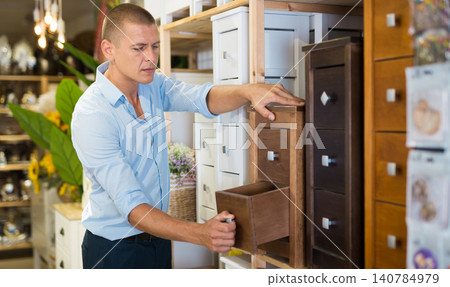 Portrait of attentive man choosing chest of drawers in furniture store Portrait of attentive man choosing chest of drawers in furniture store 140784979