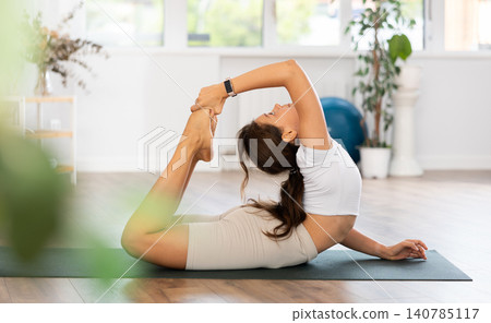 Young woman yoga trainer performing variations of bow pose on black rug Young woman yoga trainer performing variations of bow pose on black rug 140785117