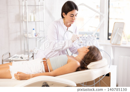 Female aesthetician applying atomized nutrients with airbrush onto woman face Female aesthetician applying atomized nutrients with airbrush onto woman face 140785130