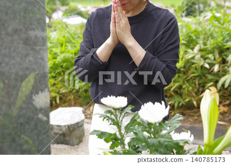 一名女子雙手合十,在墳墓前祈禱。 一名女子雙手合十,在墳墓前祈禱。 140785173