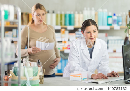 Pharmacist checking stock availability for pregnant woman with prescription Pharmacist checking stock availability for pregnant woman with prescription 140785182