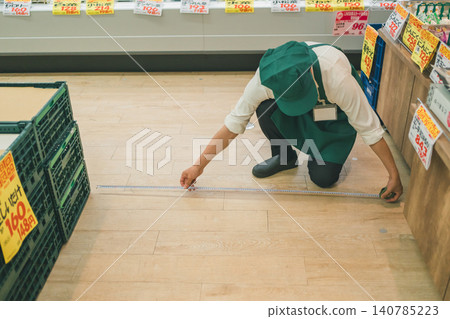 A male supermarket employee measuring the floor with a measuring tape. A male supermarket employee measuring the floor with a measuring tape. 140785223