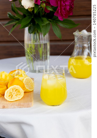 Glass of chilled lemon drink with pitcher and fresh cut lemons on white Glass of chilled lemon drink with pitcher and fresh cut lemons on white 140785225