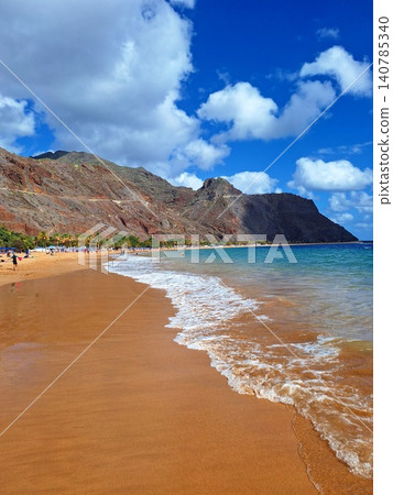 A golden dream beach in Tenerife, shimmering between turquoise waters and majestic mountain scenery. A golden dream beach in Tenerife, shimmering between turquoise waters and majestic mountain scenery. 140785340