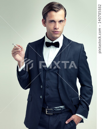 Portrait, elegant or young gentleman smoking a cigarette in studio, confidence or vintage fashion by white background. Face, serious and man in retro suit or tuxedo, bow tie and class at formal event Portrait, elegant or young gentleman smoking a cigarette in studio, confidence or vintage fashion by white background. Face, serious and man in retro suit or tuxedo, bow tie and class at formal event 140785882