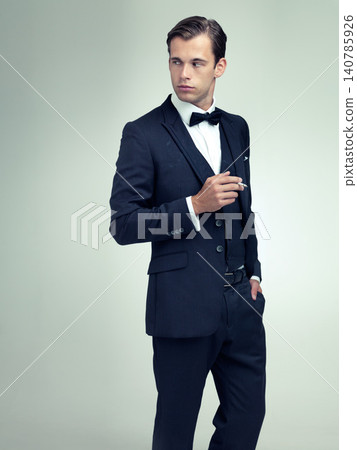 Thinking, elegant or young gentleman smoking a cigarette in studio, confidence or vintage fashion by white background. Serious, man and idea in retro suit or tuxedo, bow tie and class at formal event Thinking, elegant or young gentleman smoking a cigarette in studio, confidence or vintage fashion by white background. Serious, man and idea in retro suit or tuxedo, bow tie and class at formal event 140785926