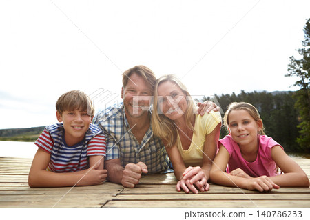 Family, portrait by lake and relax on pier outdoor for travel with vacation, parents and kids in nature for bonding. Love, support and trust with happy people and adventure together with smile Family, portrait by lake and relax on pier outdoor for travel with vacation, parents and kids in nature for bonding. Love, support and trust with happy people and adventure together with smile 140786233