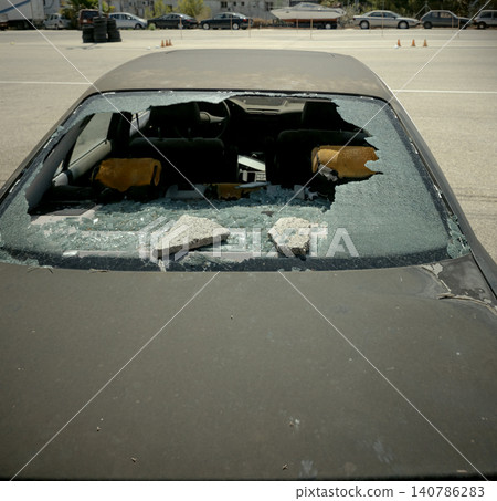 Close up view of a rear window in an abandoned car that is broken. Glass is shattered and the lot is empty. No people or activity is present, only the damaged vehicle. Close up view of a rear window in an abandoned car that is broken. Glass is shattered and the lot is empty. No people or activity is present, only the damaged vehicle. 140786283