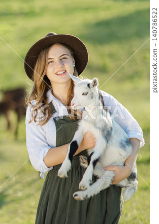 Young farmer woman holding a baby goat in her arms Young farmer woman holding a baby goat in her arms 140786522