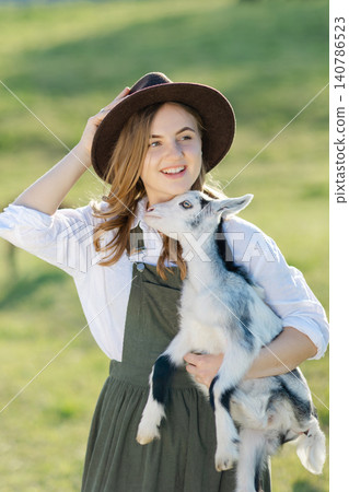 Farmer holding a baby goat in a green field Farmer holding a baby goat in a green field 140786523