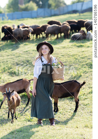 Farmer walking with goats and holding basket in front of goats herd Farmer walking with goats and holding basket in front of goats herd 140786596