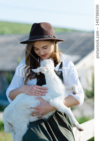 Young farmer woman holding a baby goat in a farm Young farmer woman holding a baby goat in a farm 140786600